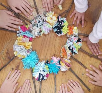 A circle of pom poms in different colours with sticks, children's hands around the circle.
