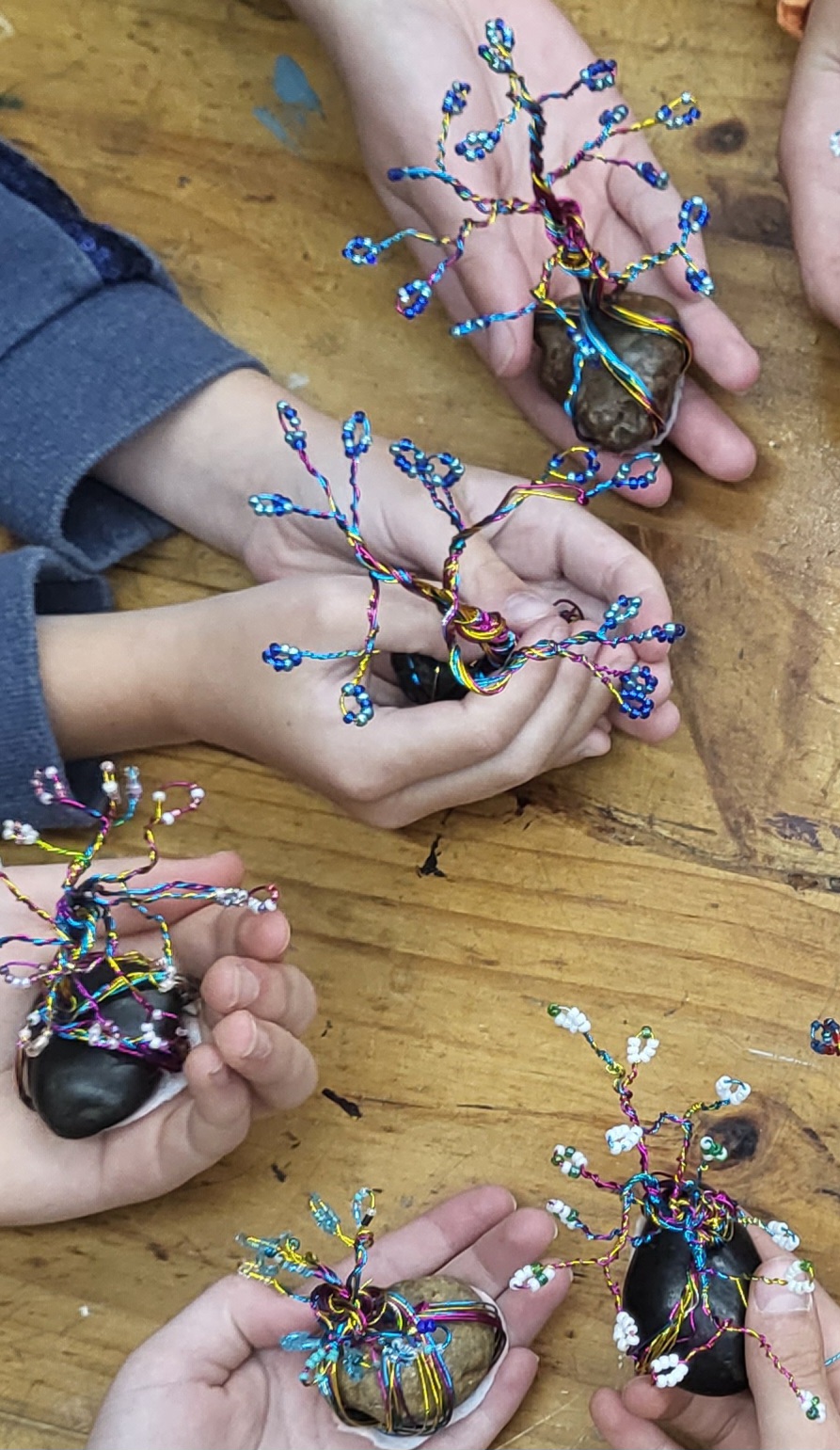 Children's hands holding Bonsai trees made with wire and beads.