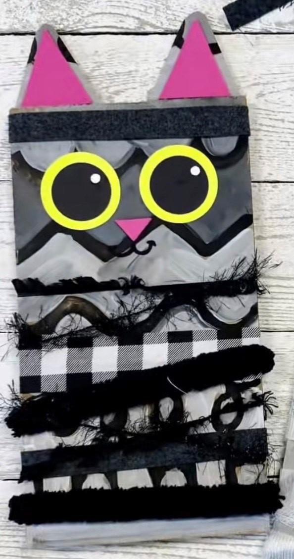 Grey, black and white materials used to make a cat with pink ears and big round yellow and black eyes.