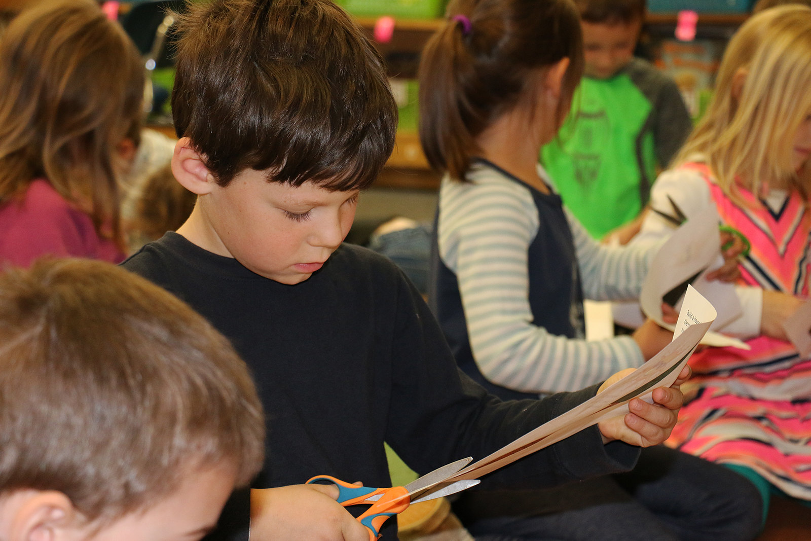 Children sitting down, cutting with scissors.