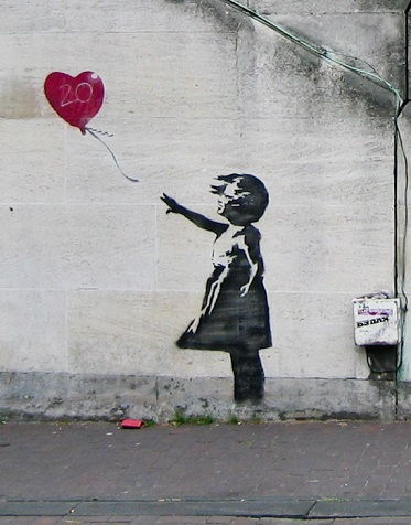 Black and white image of a young girl letting go of a red heart shaped balloon