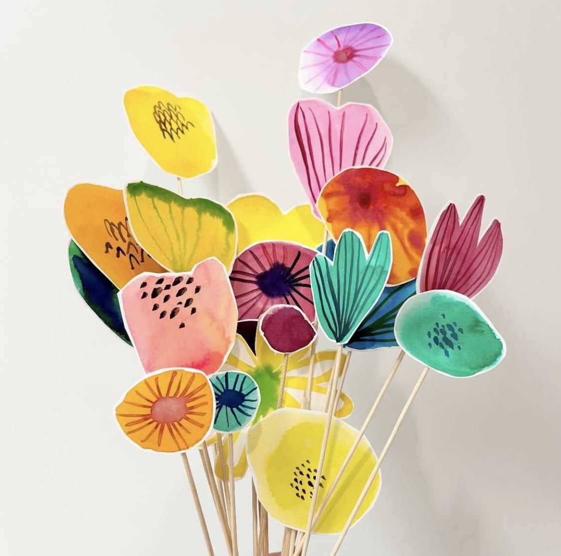 Multiple bright coloured painted flowers, all on sticks.