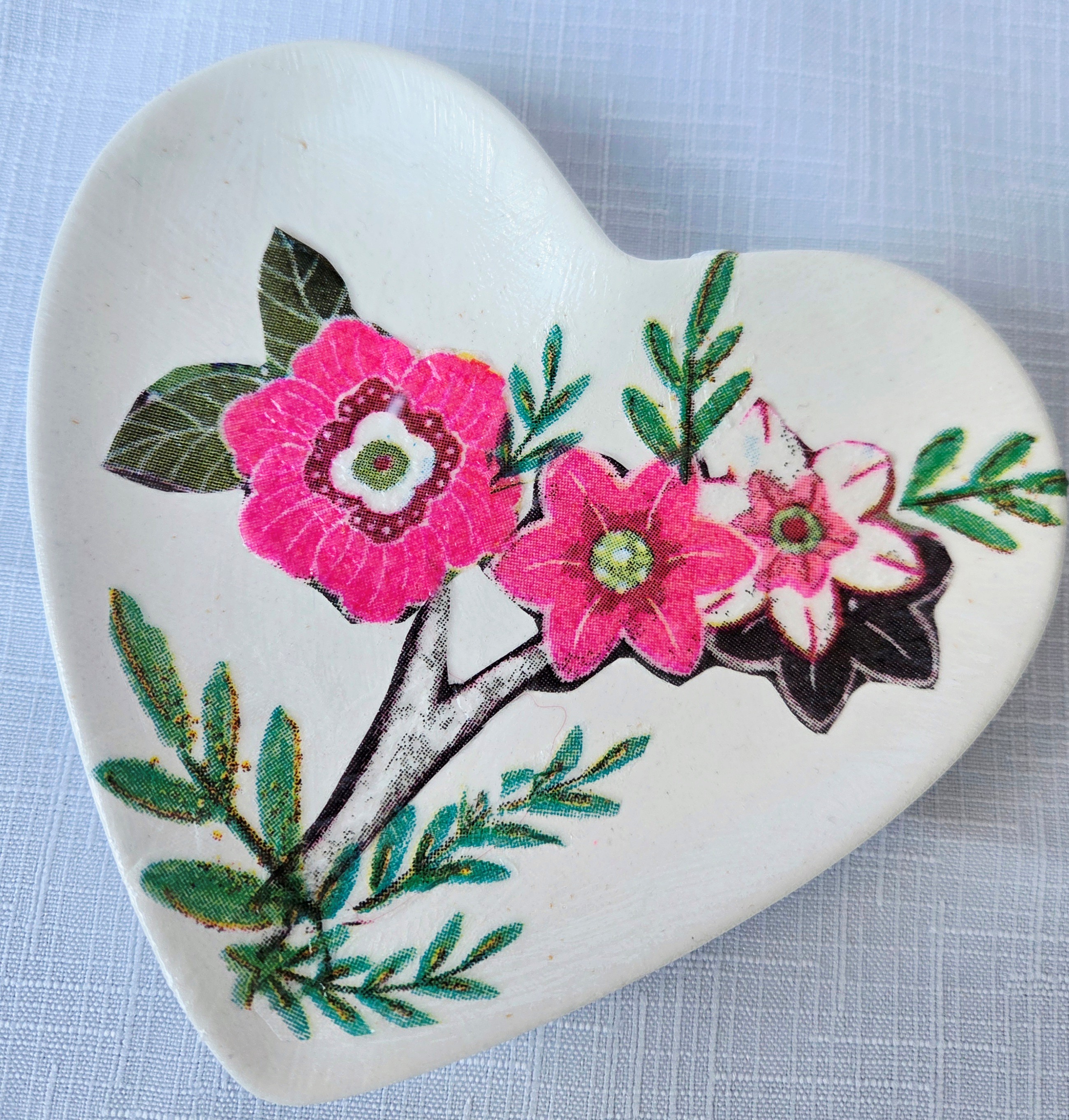 White heart shaped trinket dish with pink flowers and green leaves.