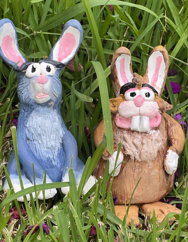Two clay rabbits, one blue and one brown sitting in the green grass