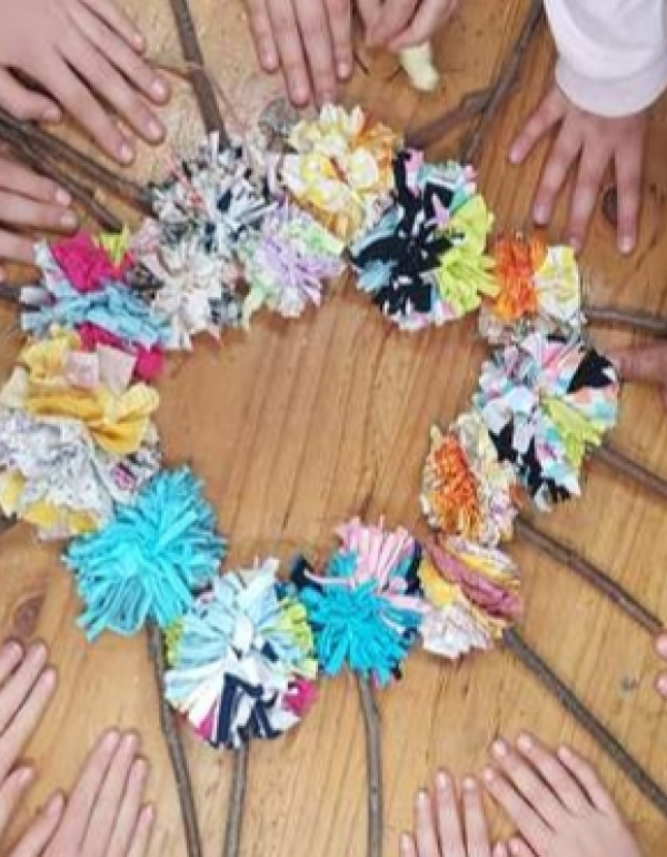 A circle of pom poms in different colours with sticks, children's hands around the circle.