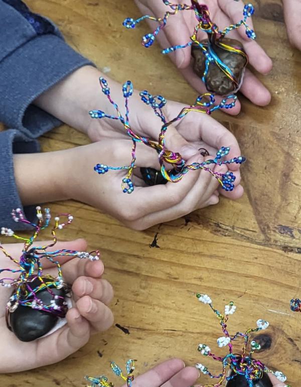 Children's hands holding Bonsai trees made with wire and beads.