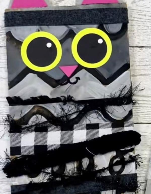 Grey, black and white materials used to make a cat with pink ears and big round yellow and black eyes.