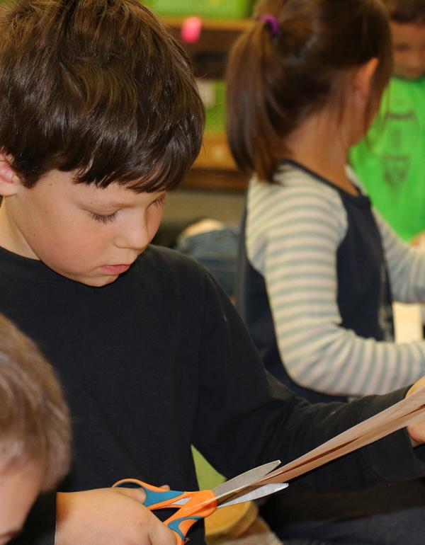 Children sitting down, cutting with scissors.