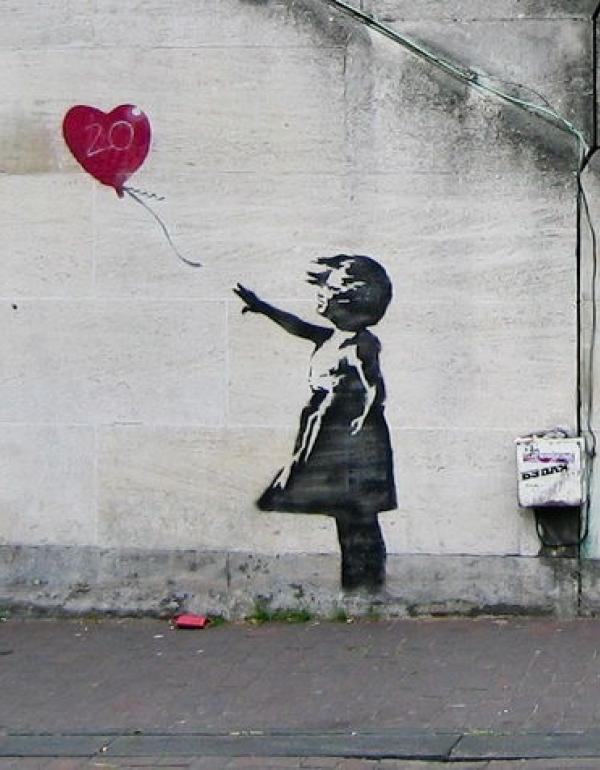 Black and white image of a young girl letting go of a red heart shaped balloon