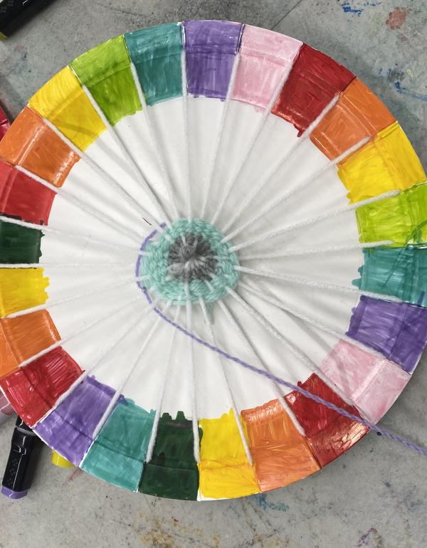 A paper plate with coloured edges used for weaving in a spiral pattern.