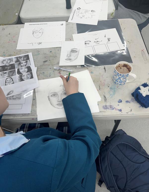 A girl drawing a face with art materials on the table
