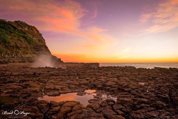 A photo taken at Avoca Beach, showing rock pools under a golden sky